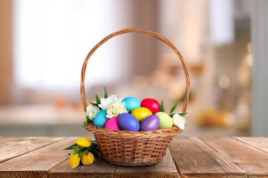 İçerideki ahşap masada parlak boyalı Paskalya yumurtaları olan hasır sepet.