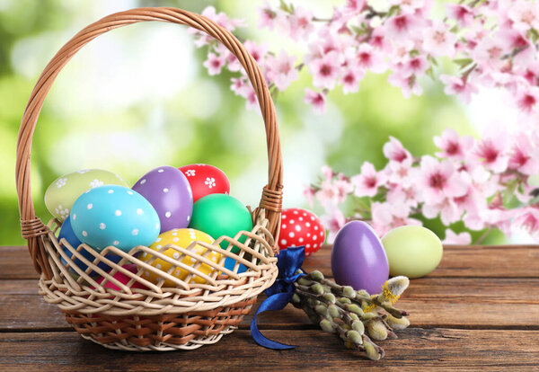 Colorful Easter eggs in wicker basket on wooden table outdoors 
