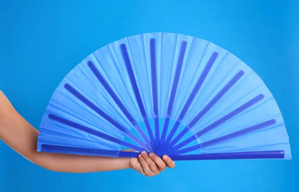 Woman holding hand fan on light blue background, closeup