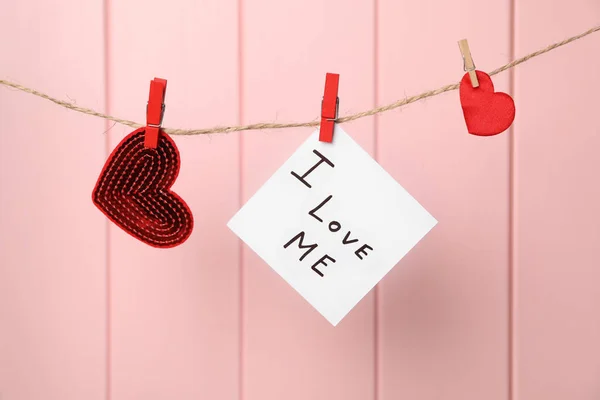 Hearts and paper note with phrase I Love Me hanging against pink wooden wall