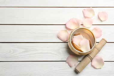 Düz kompozisyon, altın şarkı kasesi, taç yaprakları ve tokmak beyaz ahşap masa üzerinde, yazı için boşluk. İyileştirme aracı