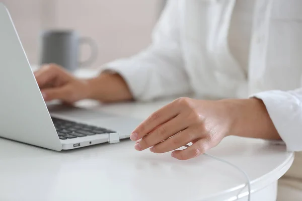 Woman connecting charger cable to laptop at white table, closeup