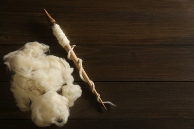 Soft white wool with spindle on wooden table, flat lay. Space for text clipart