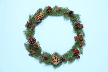 Açık mavi arka planda köknar dalları ve konilerden yapılmış Noel çelengi, üst manzara