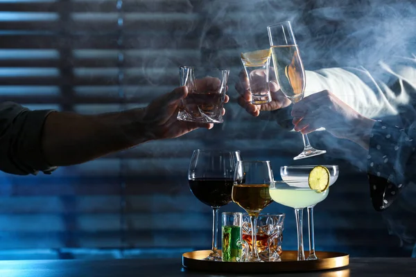 People with different alcohol drinks clinking glasses indoors, closeup