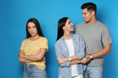 Mutsuz kadın kıskançlık hissederken çift mavi arka planda birlikte vakit geçiriyor.