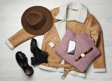 Şık botlar, yeni elbiseler, akıllı telefon ve beyaz ahşap arka planda aksesuarlar, düz yatış.