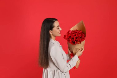 Kırmızı arka planda lale buketi olan mutlu bir kadın. 8 Mart kutlamaları