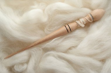 Soft white wool with spindle as background, top view clipart