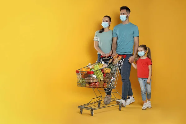 Koruyucu Maskeli Bir Aile Sarı Arka Planda Alışveriş Arabası Dolusu — Stok fotoğraf
