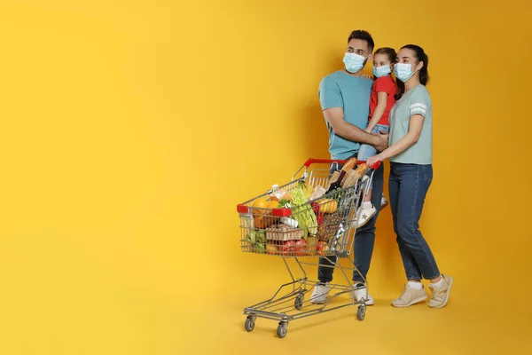 Koruyucu Maskeli Bir Aile Sarı Arka Planda Alışveriş Arabası Dolusu — Stok fotoğraf