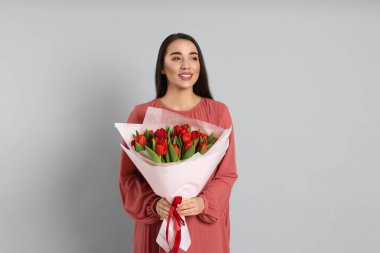 Açık gri arka planda kırmızı lale buketi olan mutlu bir kadın. 8 Mart kutlamaları