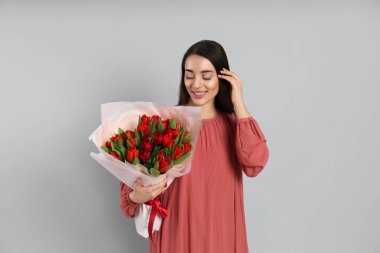 Açık gri arka planda kırmızı lale buketi olan mutlu bir kadın. 8 Mart kutlamaları