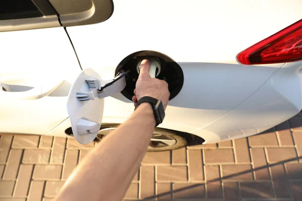 Man inserting plug into electric car socket at charging station, above view