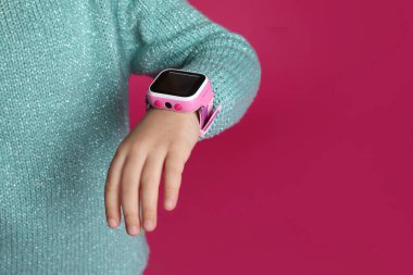 Pembe arka planda akıllı saati olan küçük bir kız, yakın plan. Metin için boşluk