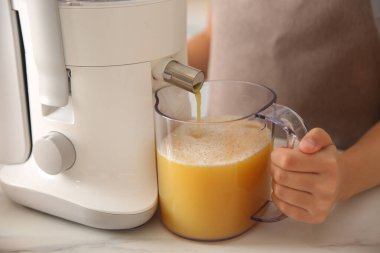 Genç bayan mutfaktaki masada taze meyve suyu yapıyor, yakın plan.