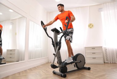 Evinde modern eliptik makine kullanan bir adam