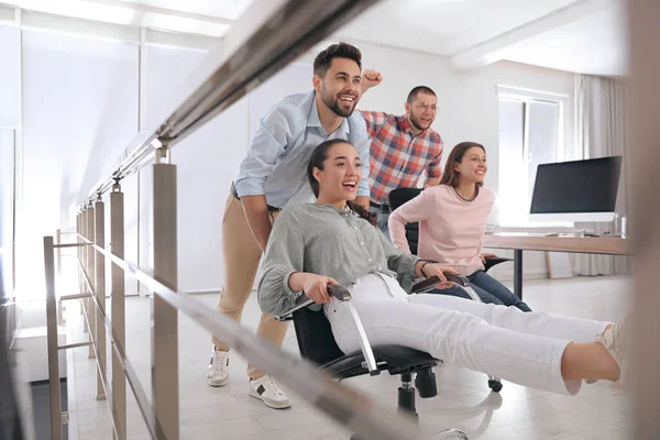 Happy office employees riding chairs at workplace