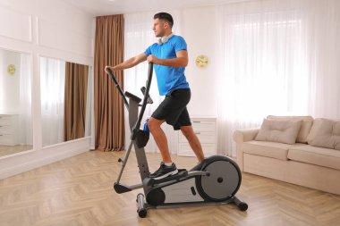 Evinde modern eliptik makine kullanan kulaklıklı bir adam.