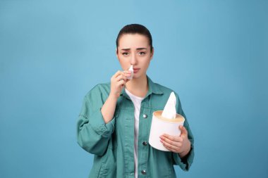 Açık mavi arka planda burun spreyi kullanan kadın.