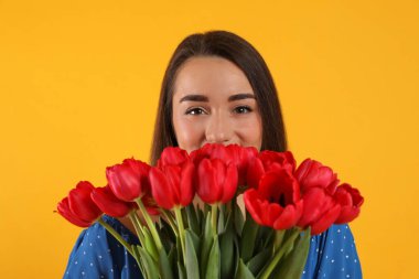 Sarı arka planda kırmızı lale buketi olan mutlu kadın. 8 Mart kutlamaları