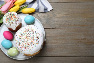 Paskalya pastaları, renkli yumurtalar ve ahşap masada laleler, düz yatak. Metin için boşluk