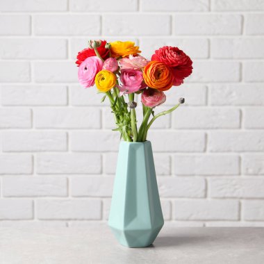 Tuğla duvarın yanındaki beyaz masada vazoda duran güzel, taze ranunculus çiçekleri.