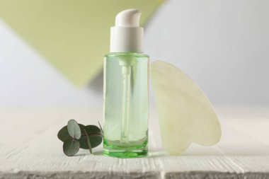 Jade gua sha aracı ve beyaz ahşap masa üzerinde cilt bakım ürünü