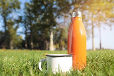 Modern turuncu termos şişesi ve fincanı yeşil çimlerin üzerinde açık havada. Metin için boşluk
