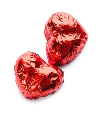Kalp şeklinde çikolata şekerlemeleri kırmızı folyoyla beyaz arka planda, üst görünümde.