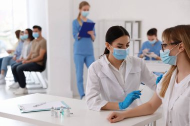 Diğerleri hastanede sırada beklerken, doktor hastaya iğne yapıyor. Aşılama kampanyası