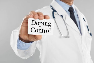 Açık gri arkaplan üzerinde Doping Kontrollü metin kartı tutan doktor, yakın plan