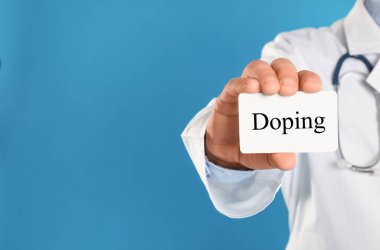 Açık mavi arka planda kelime Doping ile doktor kartı, yakın plan. Metin için boşluk