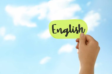 Mavi gökyüzüne karşı İngilizce kelime yazılı kağıt tutan kadın, yakın plan.