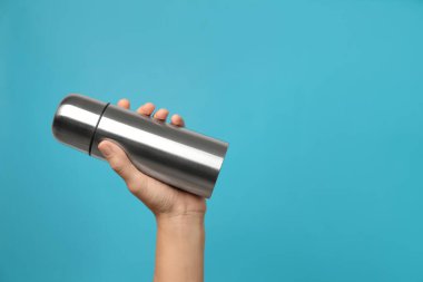 Modern termosu açık mavi arka planda tutan kadın, yakın plan. Metin için boşluk