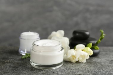 Gri masadaki kozmetik ürünleri, taşlar ve çiçeklerle güzel bir spa kompozisyonu