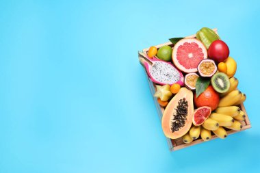 Açık mavi arka planda farklı egzotik meyveler olan sandık, üst manzara. Metin için boşluk
