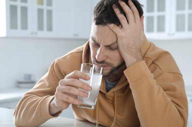 Adam mutfaktaki masada akşamdan kalmalık ilacı alıyor.