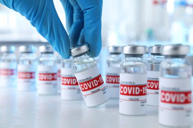 Doktor masadan COVID-19 aşısıyla cam şişe alıyor, yakın plan.