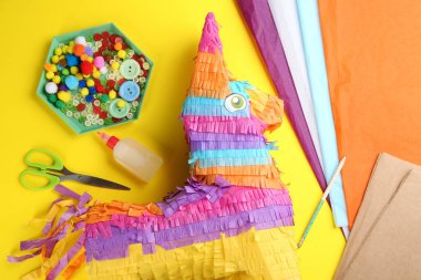 Sarı zemin üzerinde karton eşek ve malzemeler olan düz bir kompozisyon. Pinata DiY
