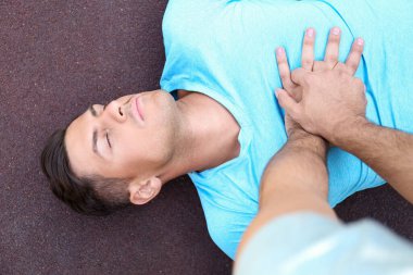 Yoldan geçen biri dışarıda baygın bir adama suni teneffüs yapıyor. İlk yardım