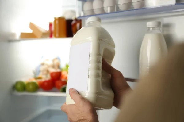 Man holding gallon of milk near refrigerator, closeup