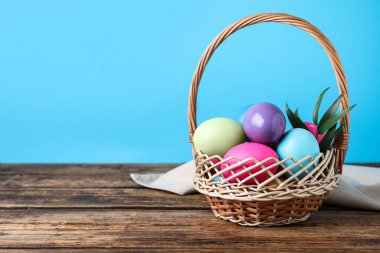 Hasır sepet içinde ahşap masada renkli Paskalya yumurtaları. Metin için boşluk