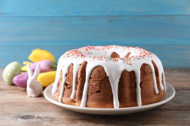 Şekerli Paskalya pastası, dekoratif tavşan, boyanmış yumurta ve ahşap masa üzerinde laleler, yakın plan.