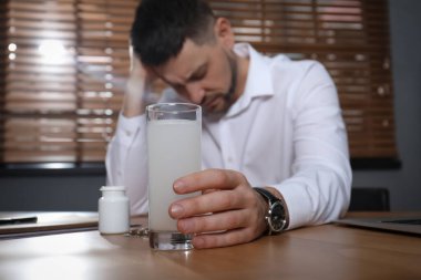 Ofiste akşamdan kalmalık ilacı alan adam, elinde camla eline odaklan.