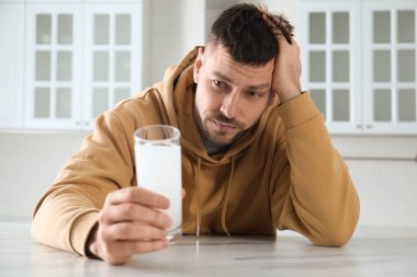 Adam mutfaktaki masada akşamdan kalmalık ilacı alıyor.