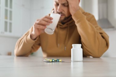 Adam mutfakta akşamdan kalmalık ilacı alıyor, haplı şişeye odaklanıyor.