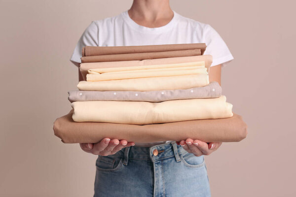 Женщина держит стопку чистого постельного белья на бежевом фоне