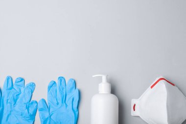 Tıbbi eldivenler, solunum maskesi ve gri arka planda el dezenfektanı. Metin için boşluk