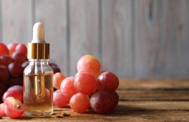 Organik kırmızı üzümler, tohumlar ve ahşap masanın üzerinde doğal bir yağ şişesi. Metin için boşluk